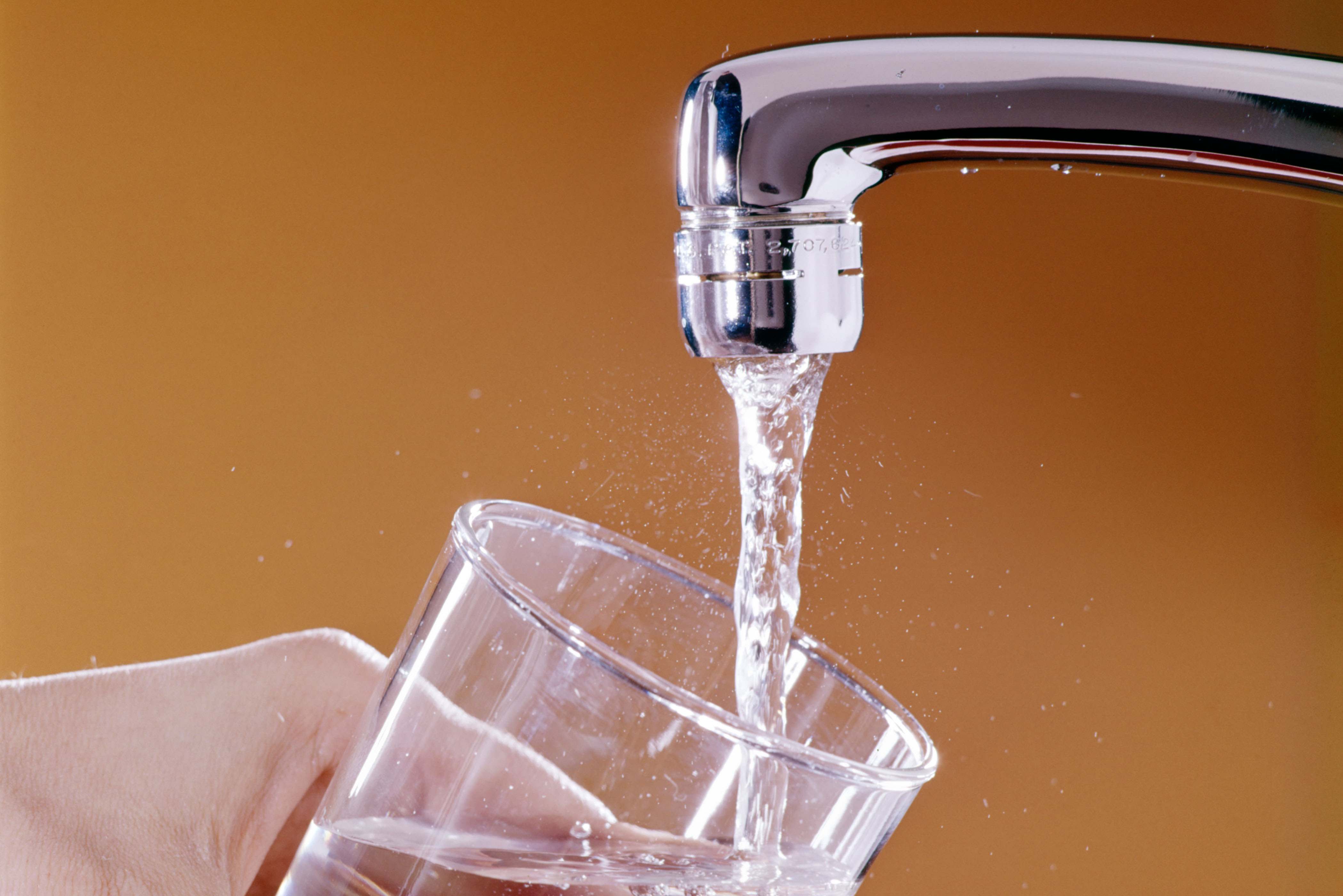 Water pouring from a faucet into a drinking glass.