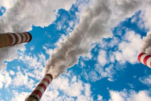 smokestacks billowing pollution into a blue sky dotted with white clouds